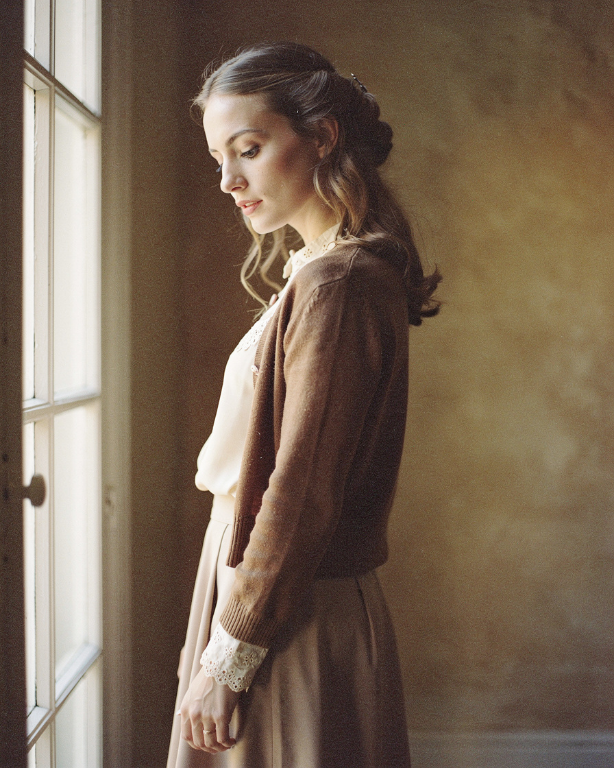 Vertical portrait of a woman in vintage attire beside a window